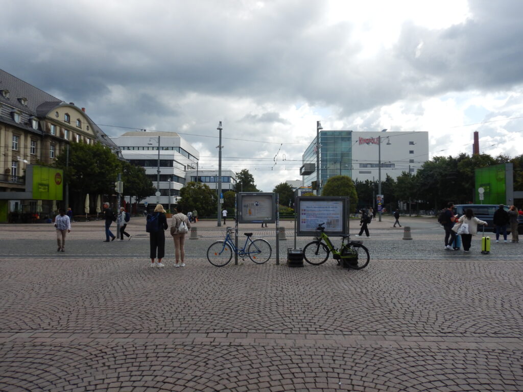 Bahnhofvorplatz vom Hauptausgang aus: Stadtmobiliar, Personen, im Hintergrund Gebäude)