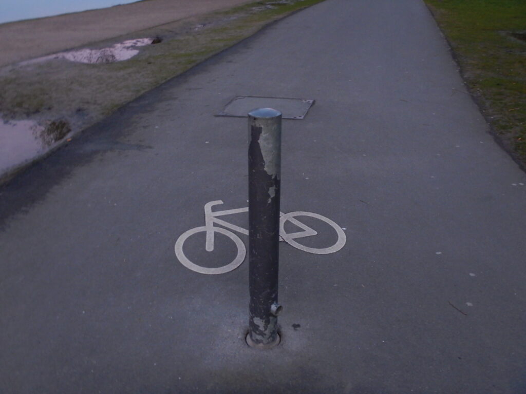 Ein grauer Pfosten steht vor einem Radpiktogramm auf grauem Asphalt