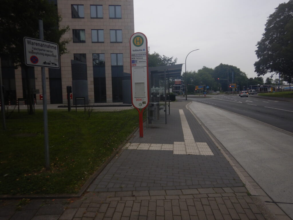 Bushaltestelle mit einem Unterstand auf der linken Seite, im Vordergrund das Haltestellenschild