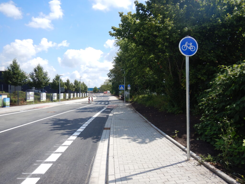 Rechts Verkehrszeichen 237 Radweg, nach links folgen der Gehweg, ein schmaler Streifen Fahrbahn, eine gestrichelte Linie und der Rest der Fahrbahn