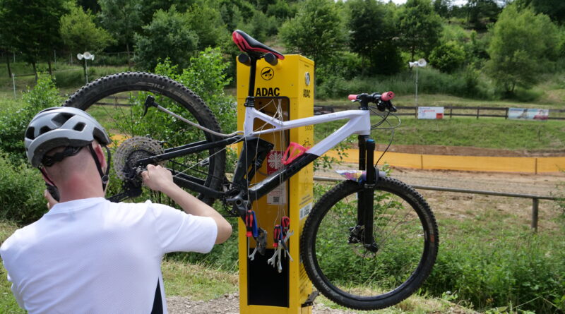 An der Servicestation hängt ein Mountain-Bike. Ein Mann wartet das Rad. Er ist von hinten zu sehen links im Bild.