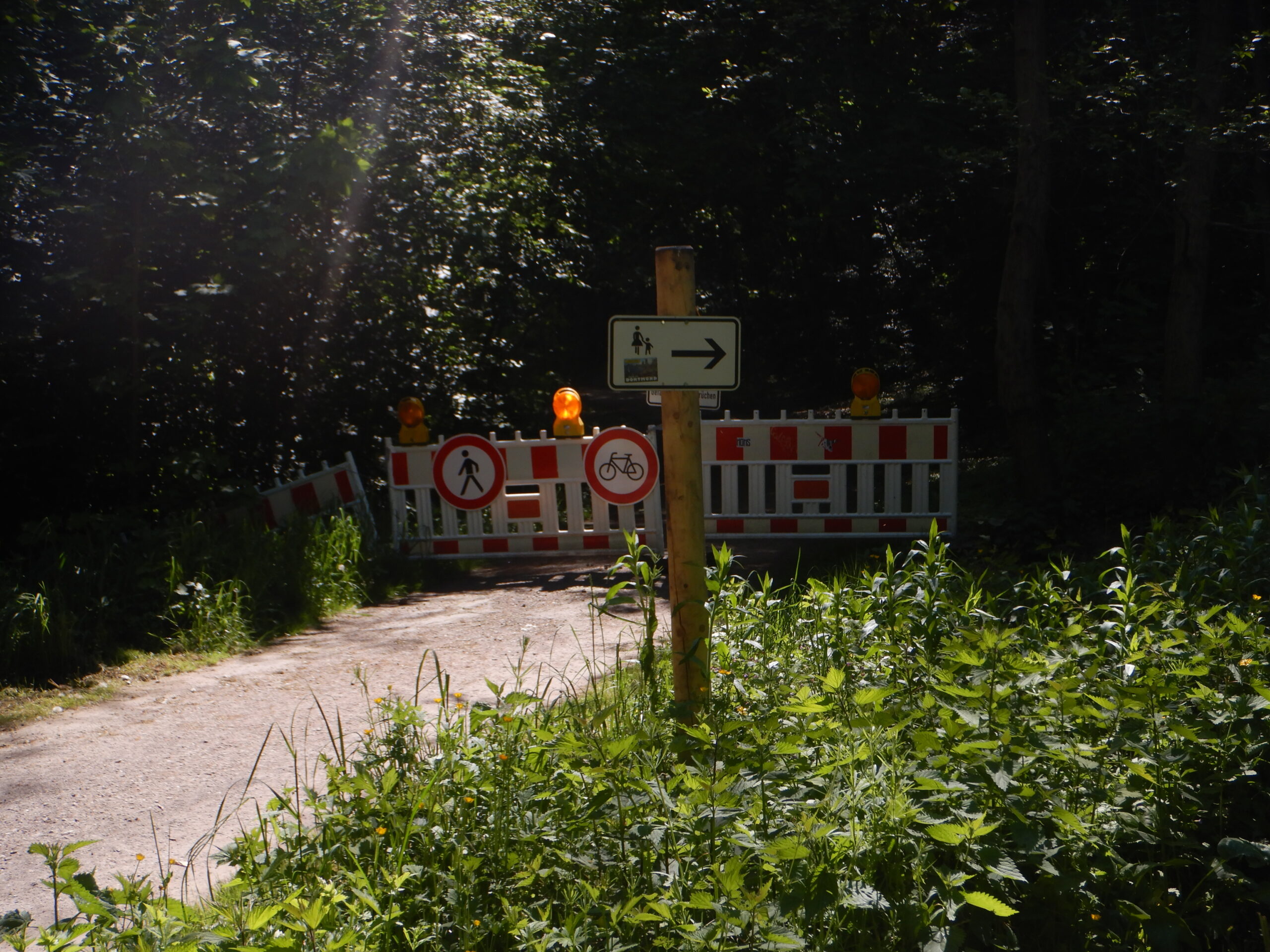 Im Hintergrund die Sperrung des Weges, im Vordergrund ein weißes Schild.