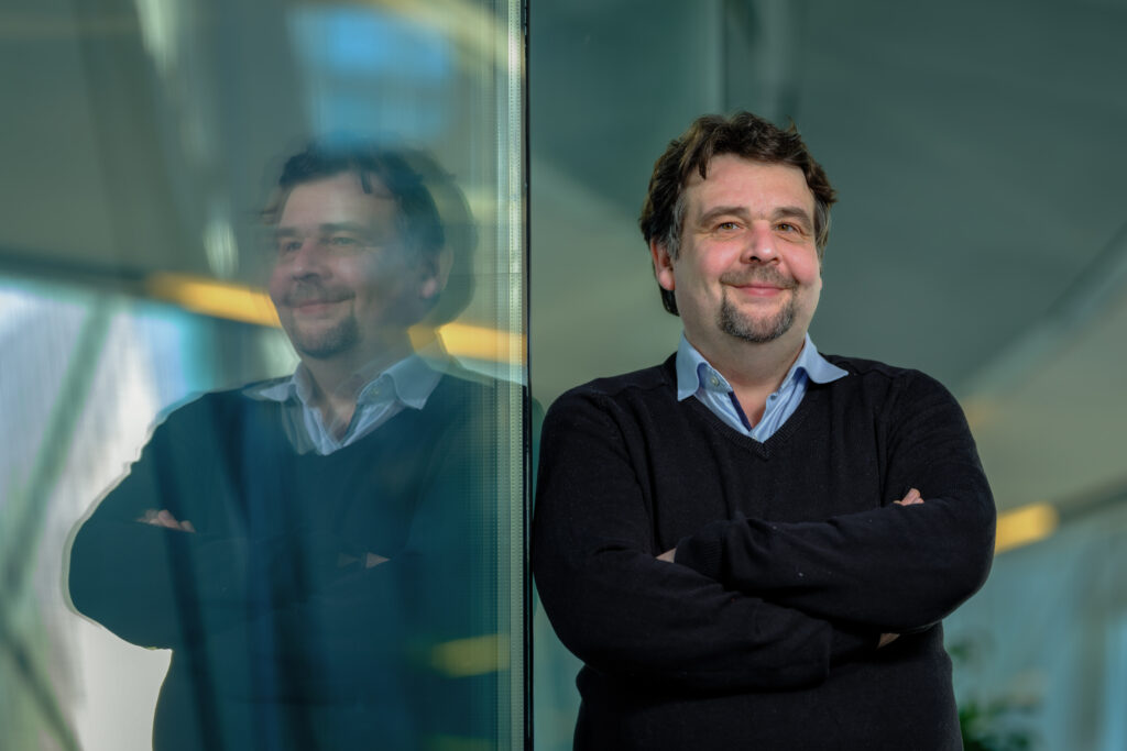 Im rechten Bildteil sieht man Oberkörper und Kopf von Dennis Radtke. Im linken Bildteil spiegelt er sich in einem Fenster.